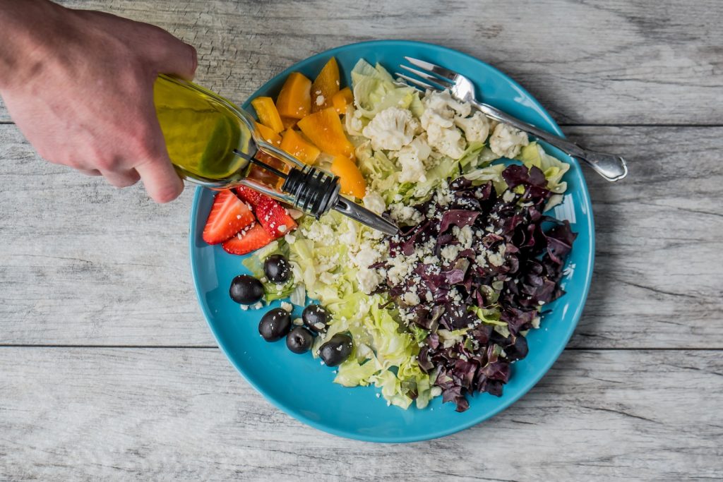 Une personne verse de l'huile d'olive sur une assiette de salade dans le but de manger des lipides.